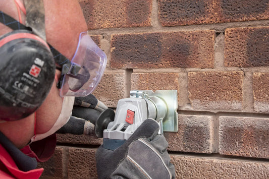Raking out a mortar joint with an angle grinder and dust extraction guard, operator wearing ear defenders and safety glasses