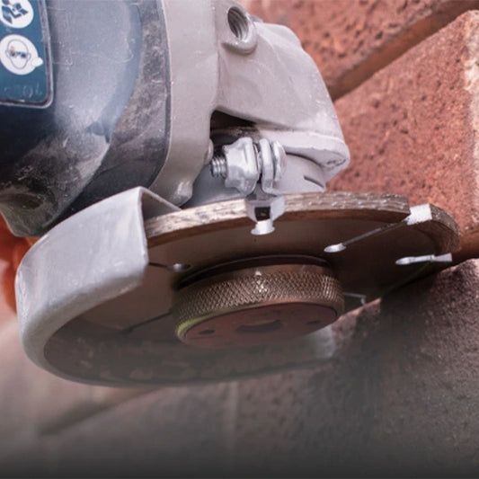 Close-up of a mortar raking disc attached to an angle grinder, cutting into brick mortar joints for removal during wall renovation.