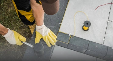 Landscaper wearing gloves using a rubber mallet to install paving stones, with a measuring string and spool on the ground.