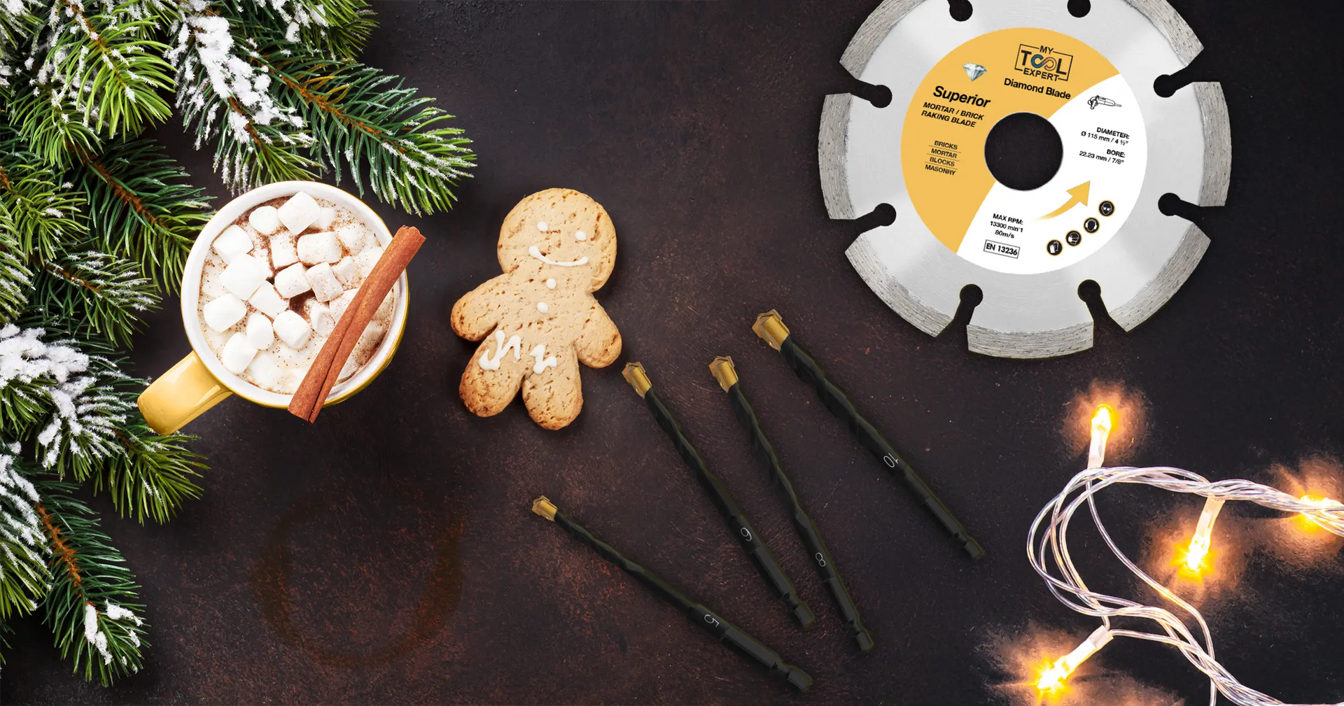 Festive Christmas flat lay with gingerbread, hot chocolate, lights, evergreen branches, and a diamond cutting blade, blending holiday warmth with craftsmanship